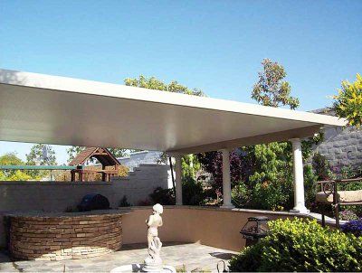 Patio with a white roof supported by columns, overlooking a yard with greenery and a stone wall.