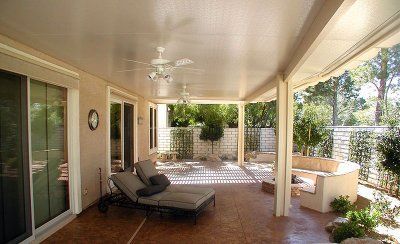 Patio with lounge chairs, ceiling fan, and sliding glass doors. Brown flooring, tan walls, and a view of greenery.