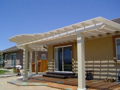 Beige pergola attached to a house with a sliding glass door and a person working nearby.