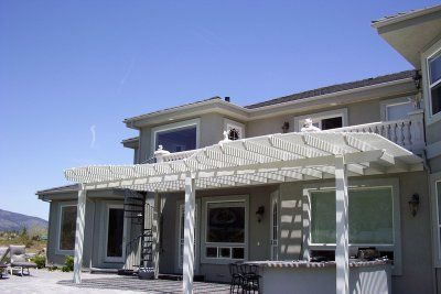 White pergola attached to a light-colored house with a blue sky background.