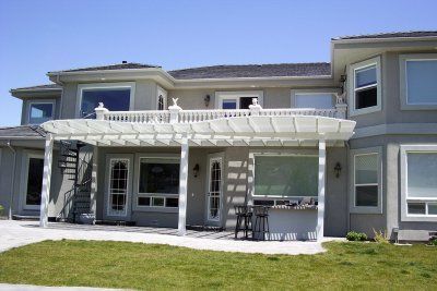 Two-story beige house with white pergola over patio and small grassy yard.