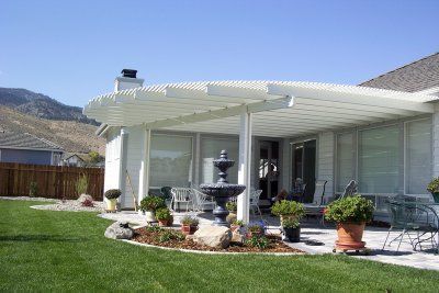 White pergola over a patio with a fountain and potted plants in a backyard.