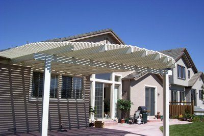 Beige patio cover over a patio, with a house in the background and a blue sky.