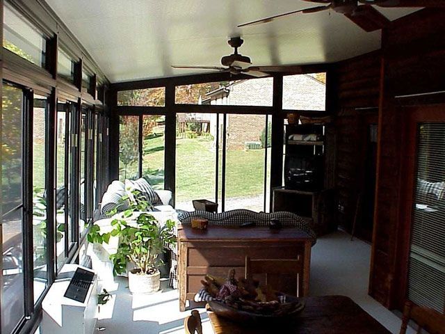 Sunroom interior with dark wood trim, large windows, and a view of a grassy yard.