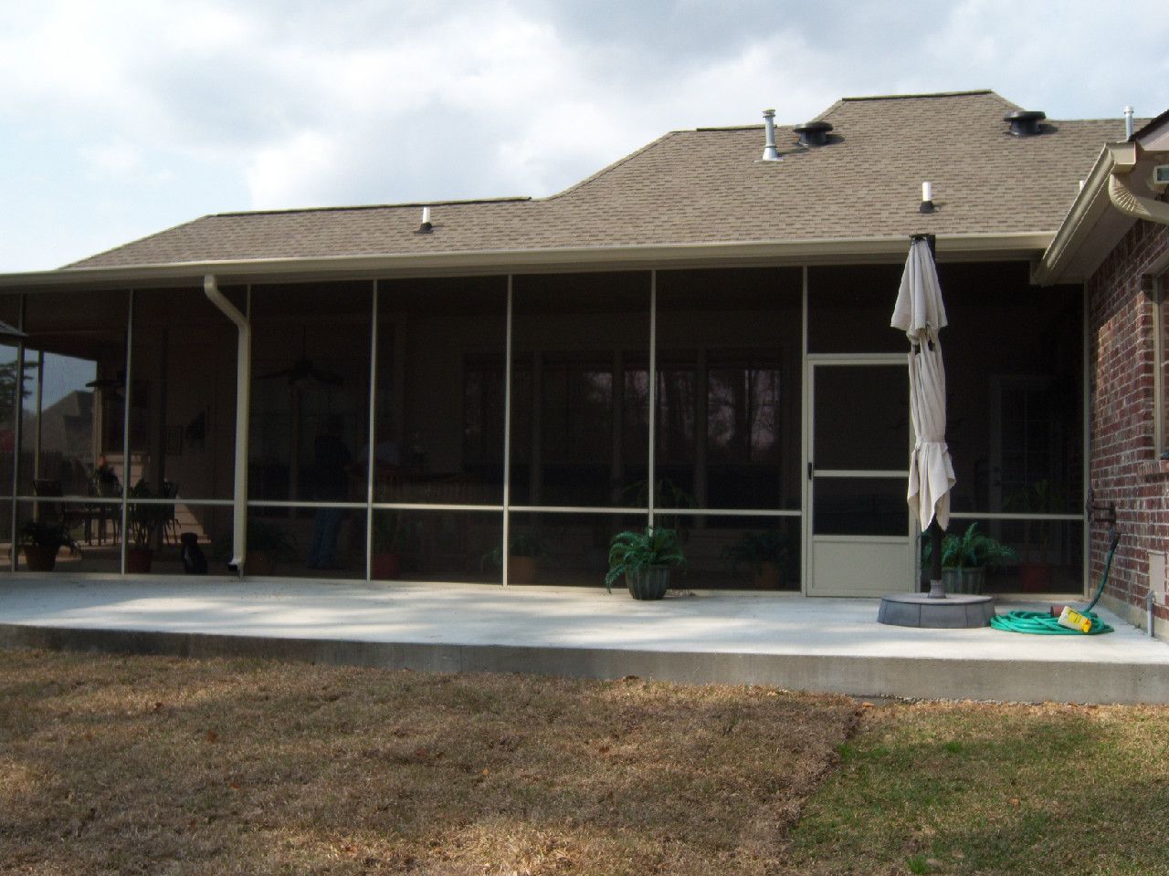 Screened-in patio with a concrete floor, umbrella, and view of a home's exterior, brown and beige tones.