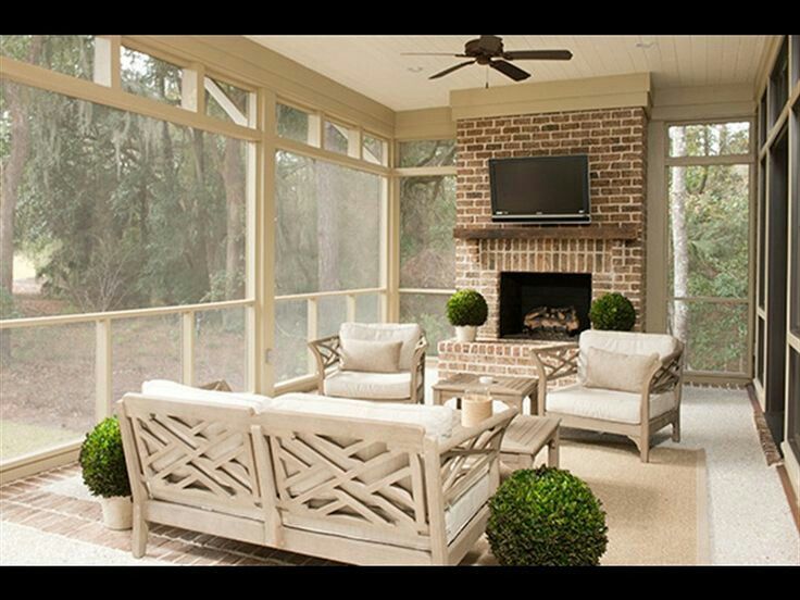 Screened-in porch with light-colored furniture, brick fireplace, and television. Overlooks a natural landscape.