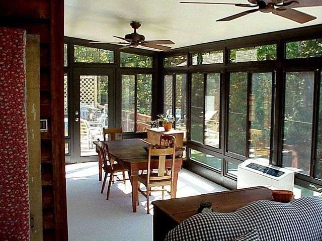 Sunroom with large windows, dining table, chairs, and ceiling fans. Bright sunlight illuminates the room.