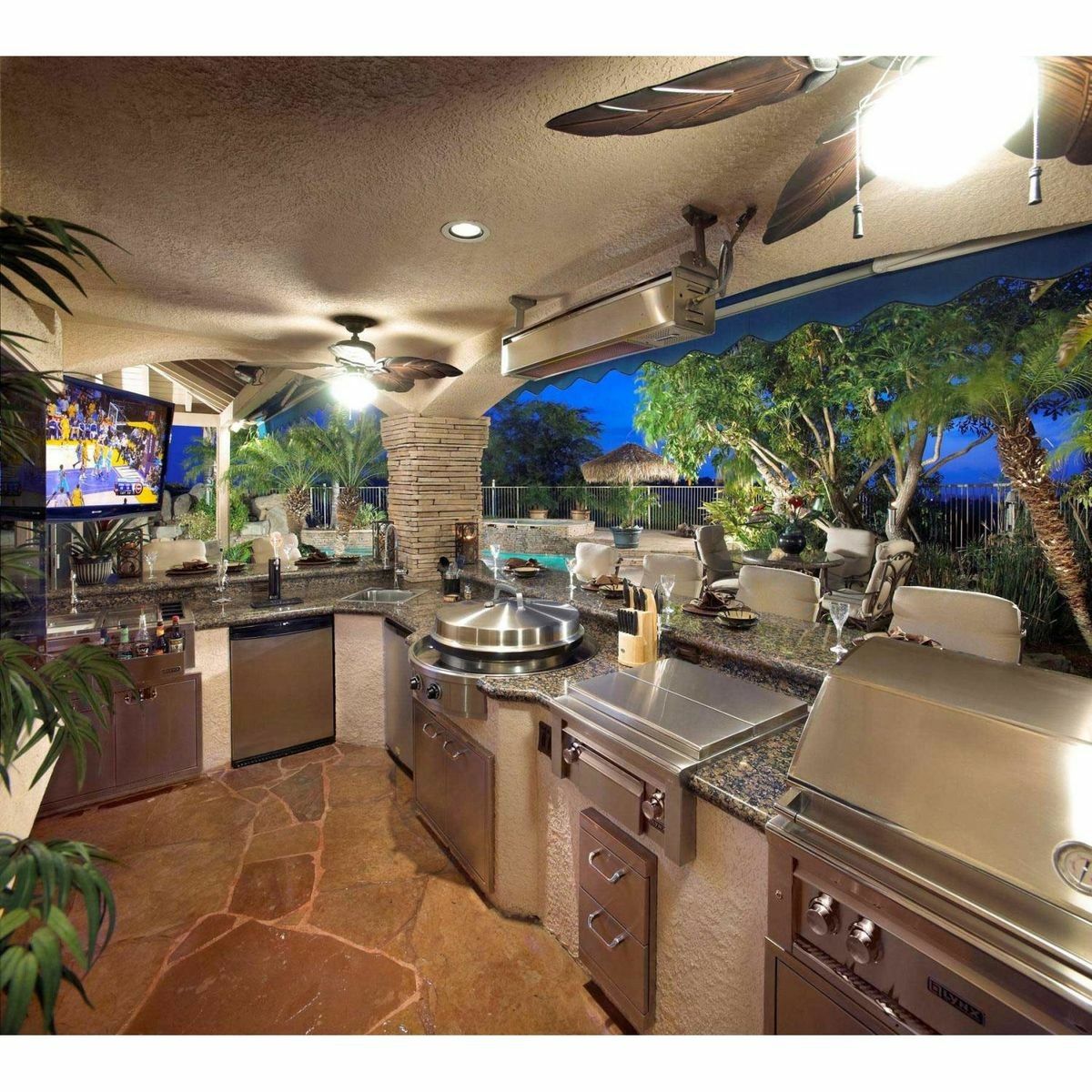 Outdoor kitchen with stainless steel appliances, granite countertops, and a television.