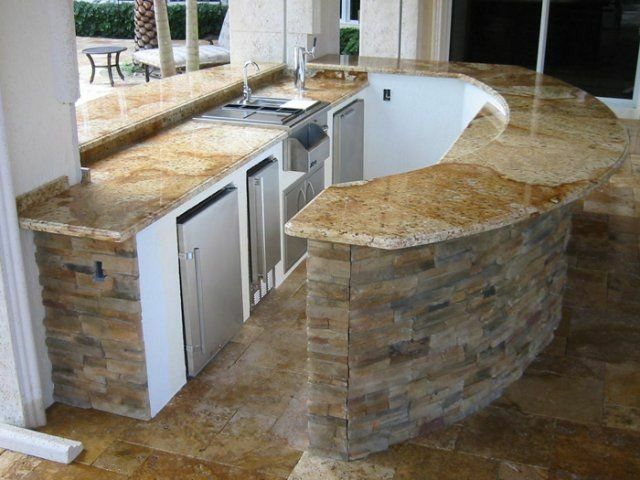 Outdoor kitchen with granite countertops, stone facade, and appliances.