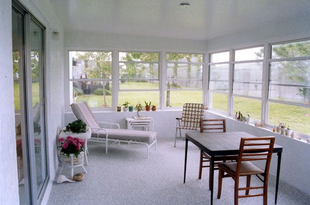 Sunroom with white walls, windows, and patio furniture overlooking a grassy yard.