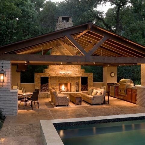 Outdoor living space with pool, fireplace, seating, and grill under a wooden roof.