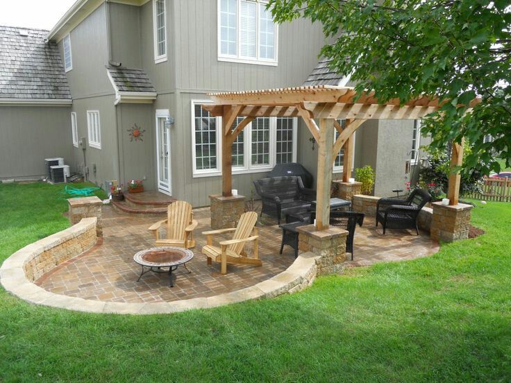 Backyard patio with wooden pergola, seating, fire pit, and grill. House exterior in background.