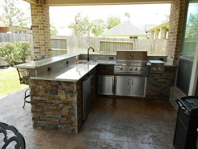 Outdoor kitchen with granite countertops, stone accents, and stainless steel appliances.