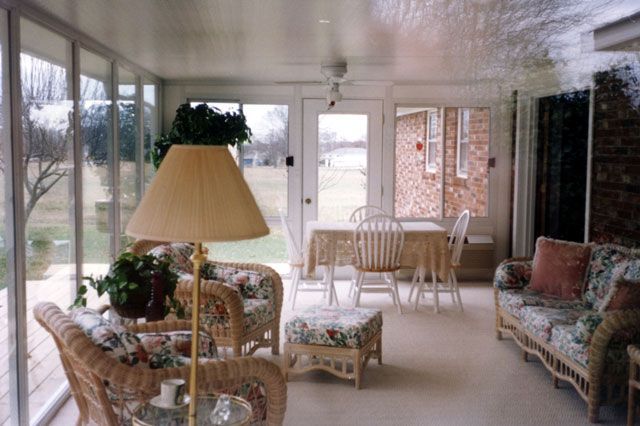Sunroom with wicker furniture, a table, and windows overlooking a grassy yard.