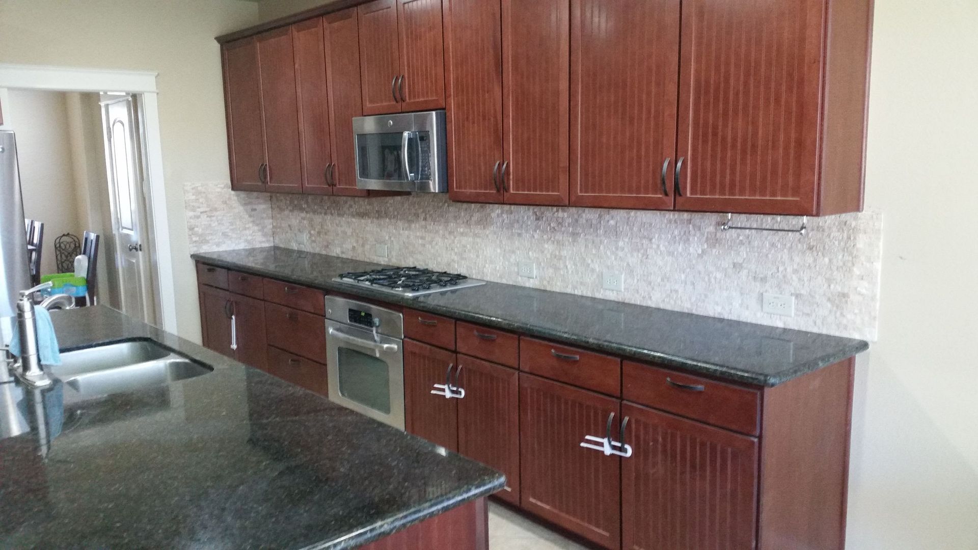 Kitchen with dark cabinets, black countertops, and a stone backsplash