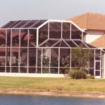 Screened-in porch attached to a house with a tan roof, next to a lake