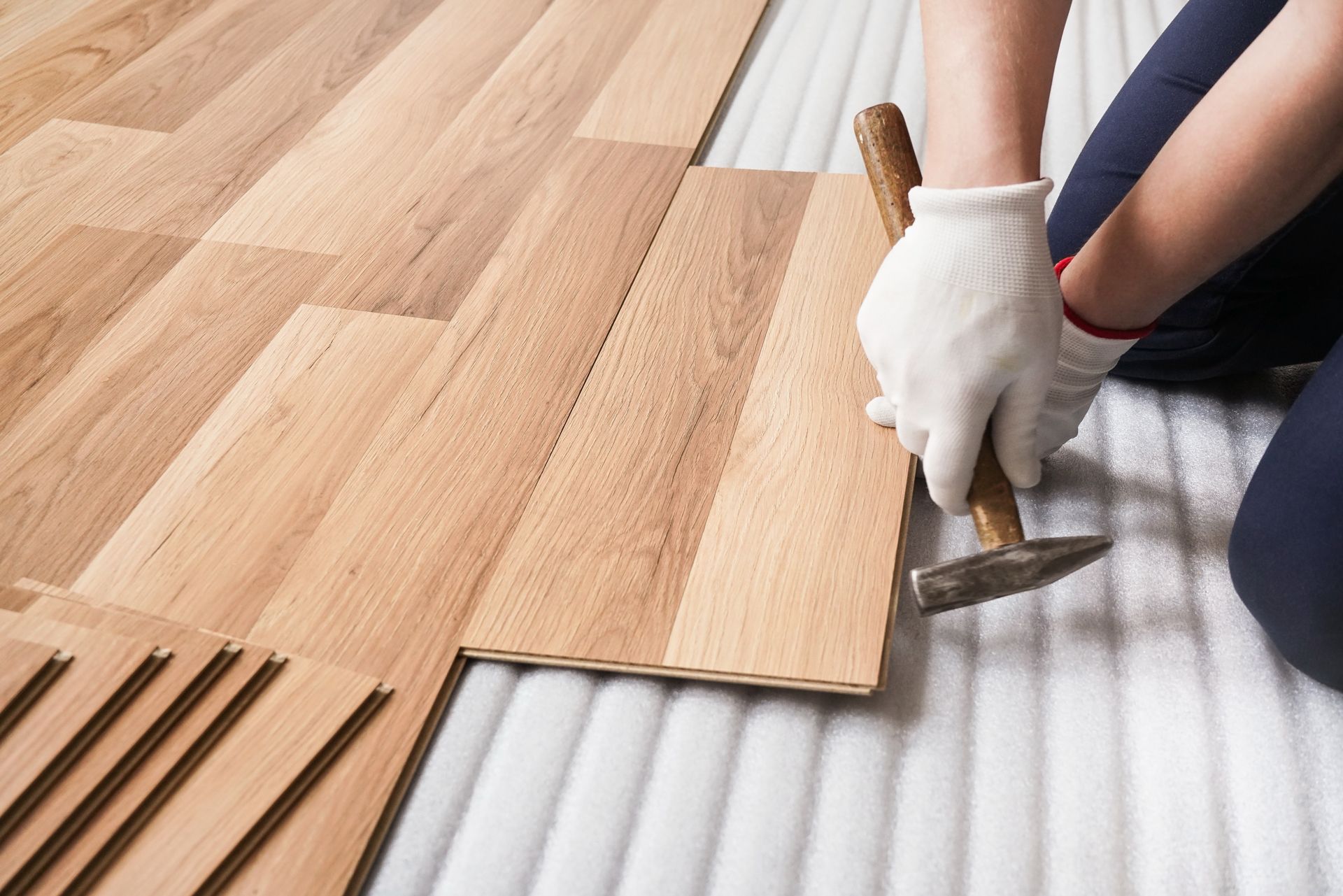 Person installing wood flooring with a hammer and wearing gloves