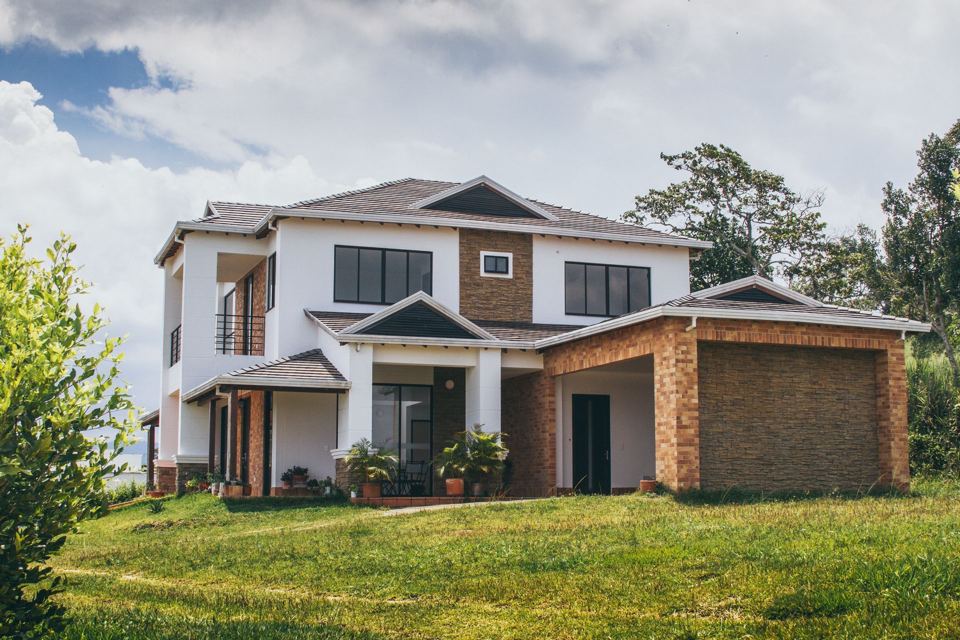 Two-story house with white walls, a brick garage, and a green lawn under a cloudy sky.