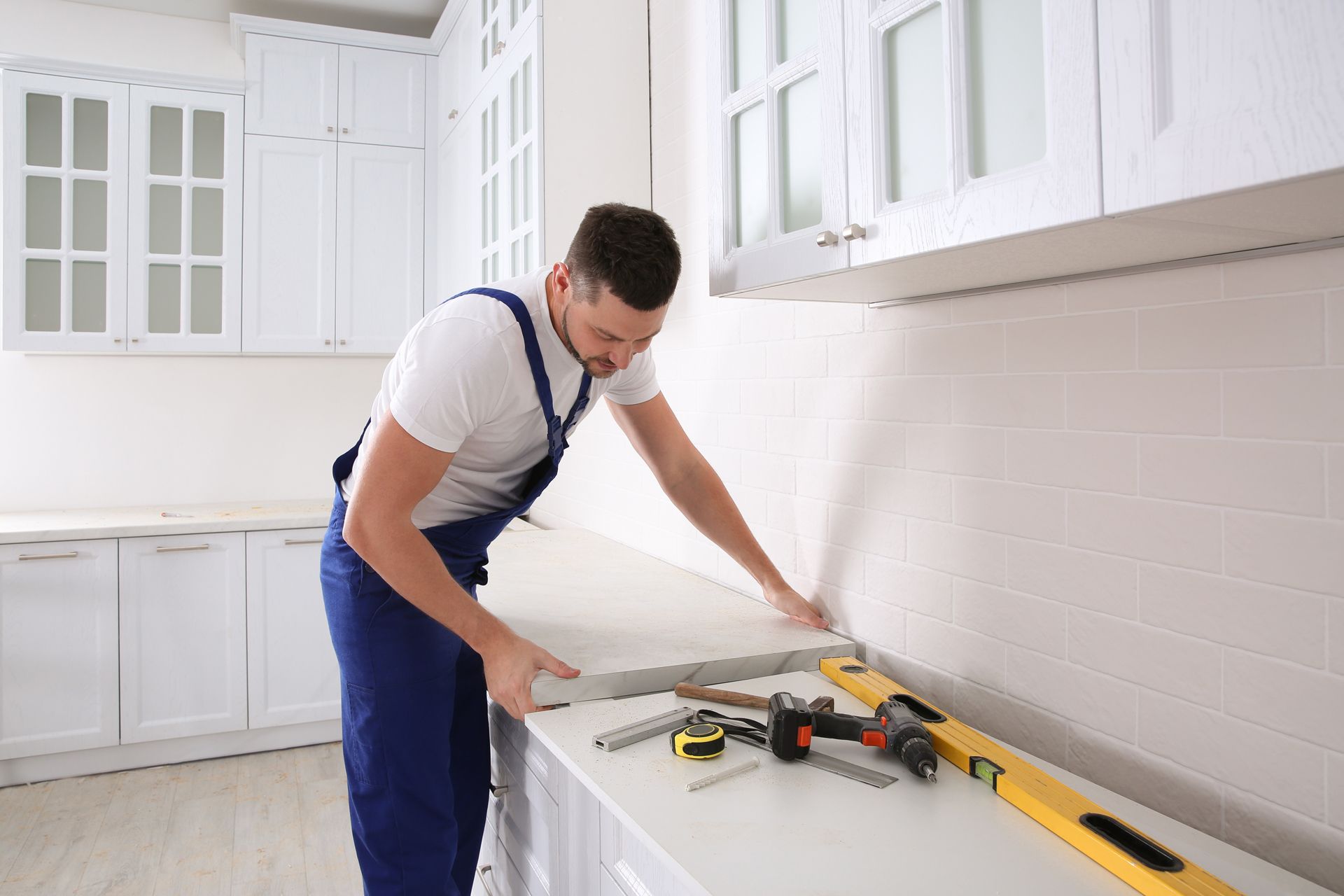 Man installing a countertop in a white kitchen, with tools on the surface