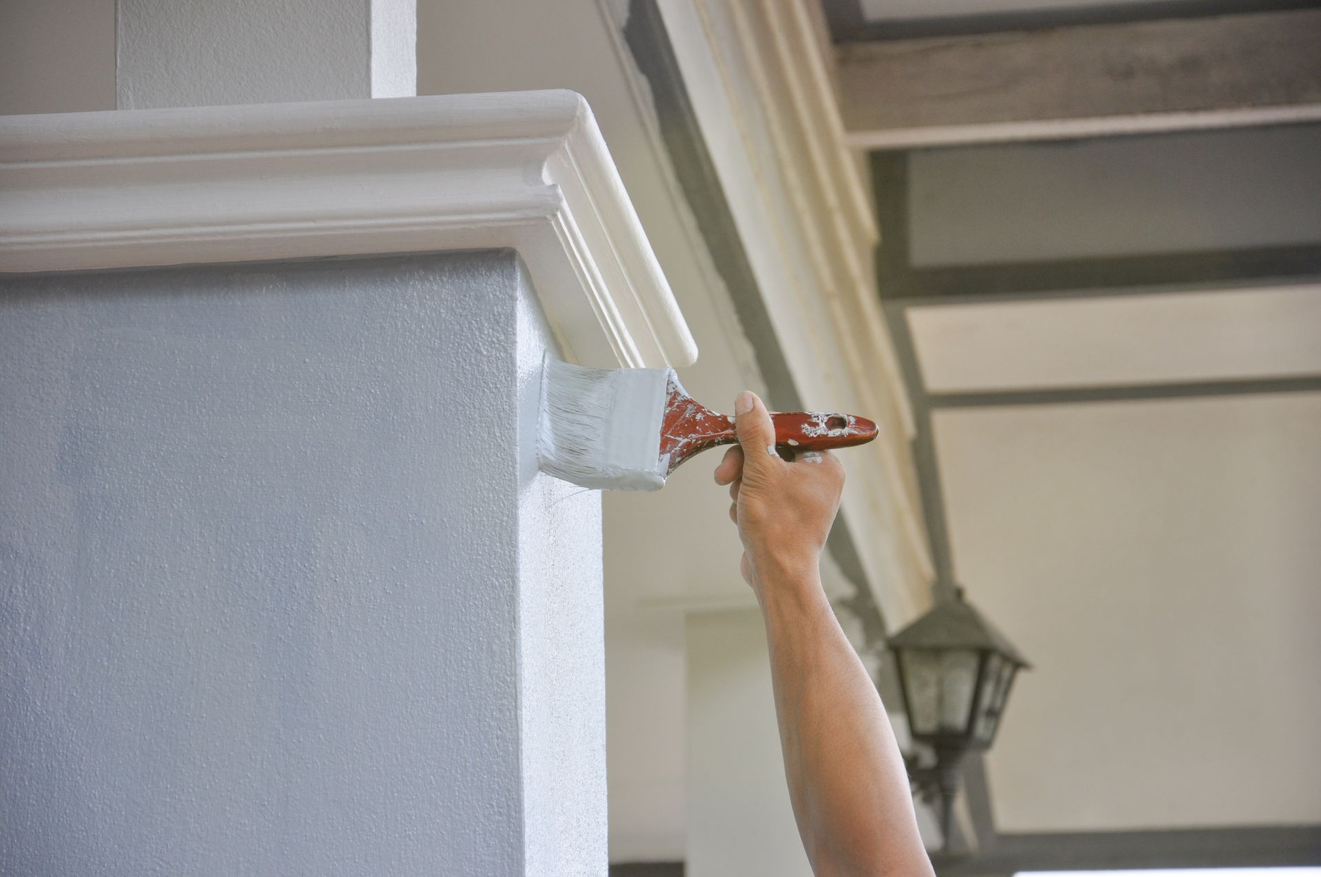 Person painting white trim on a gray pillar outdoors.