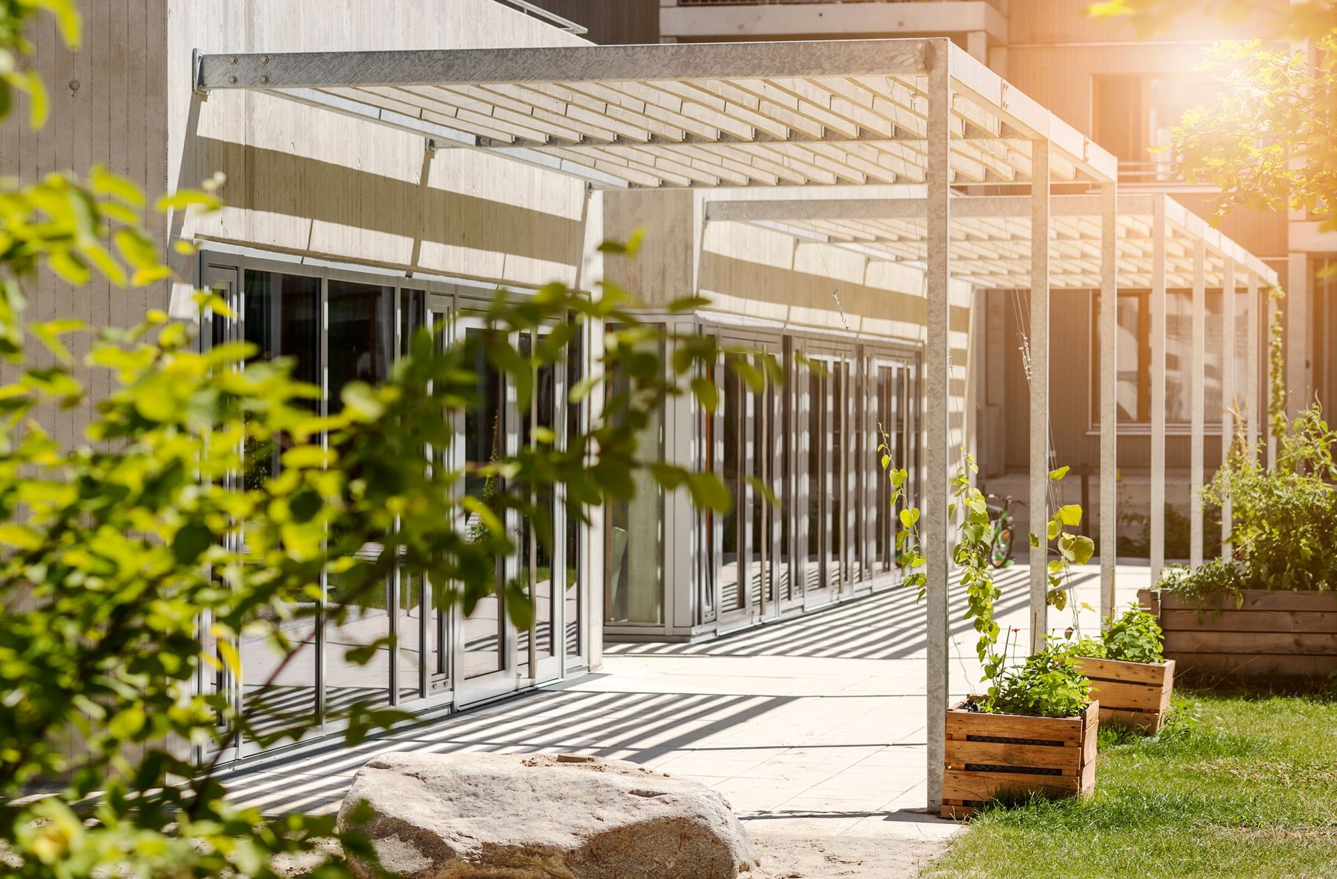 Pergola over outdoor patio with planters and building with glass doors