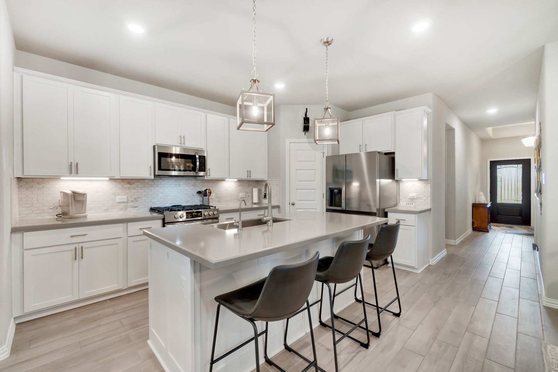 Modern white kitchen with island, stainless steel appliances, and gray stools