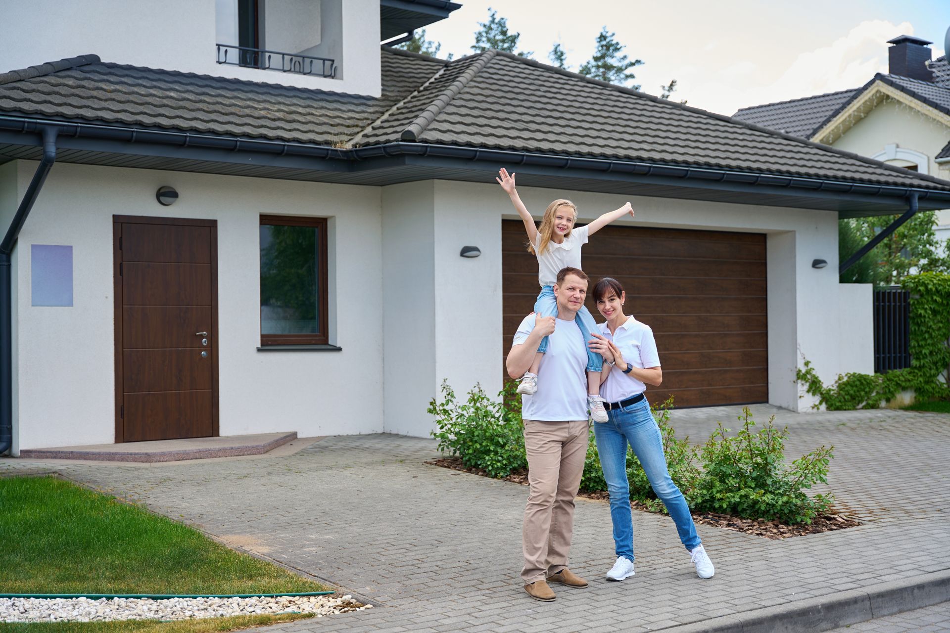 Family of three outside a house, daughter on father's shoulders with arms raised