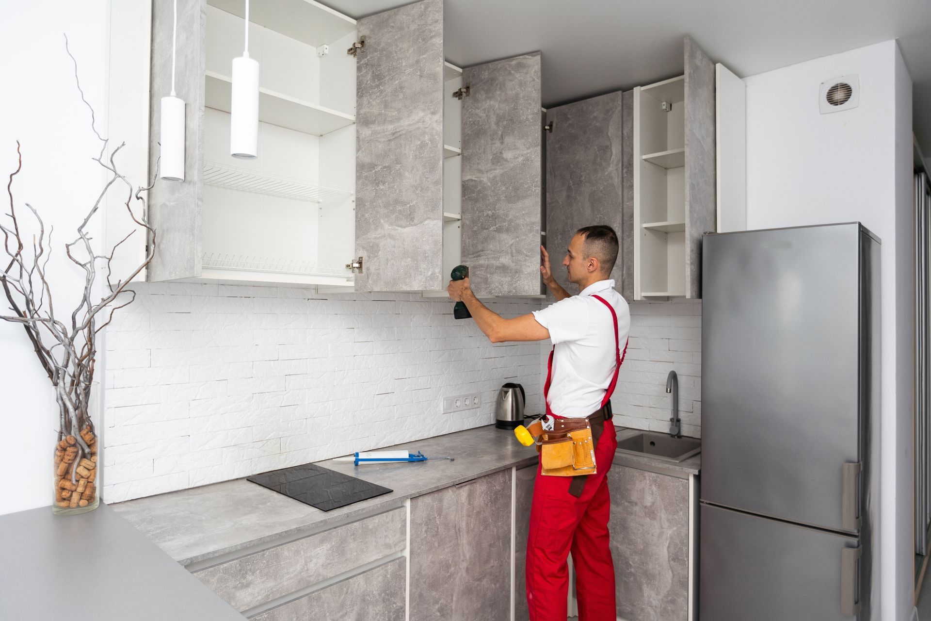Person installing kitchen cabinet, countertop, backsplash, and fridge