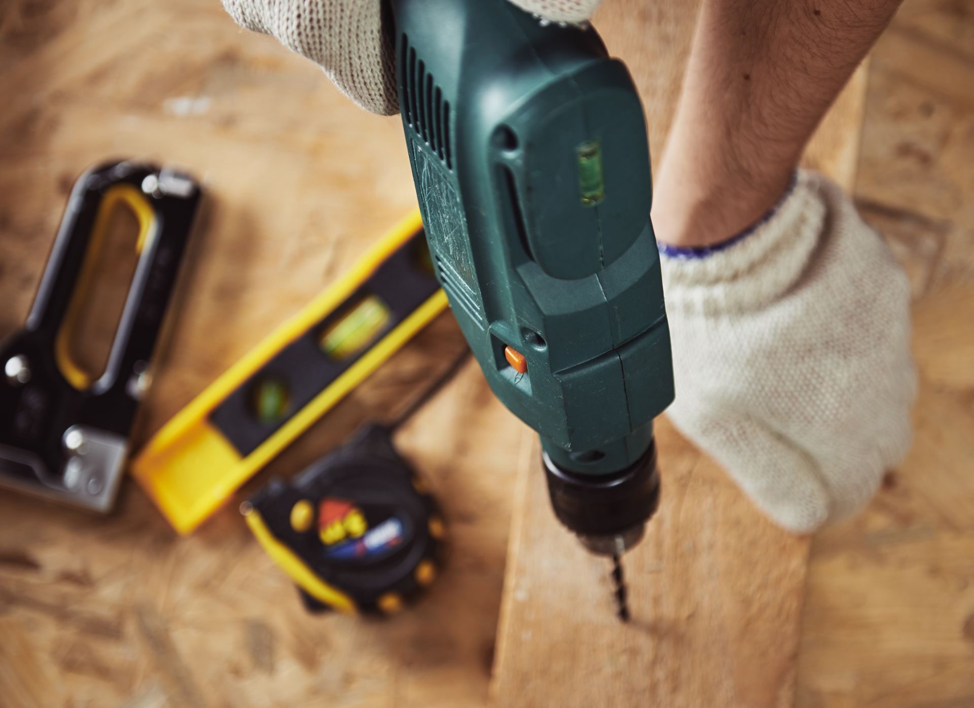 Person using a power drill on a wooden surface, wearing work gloves