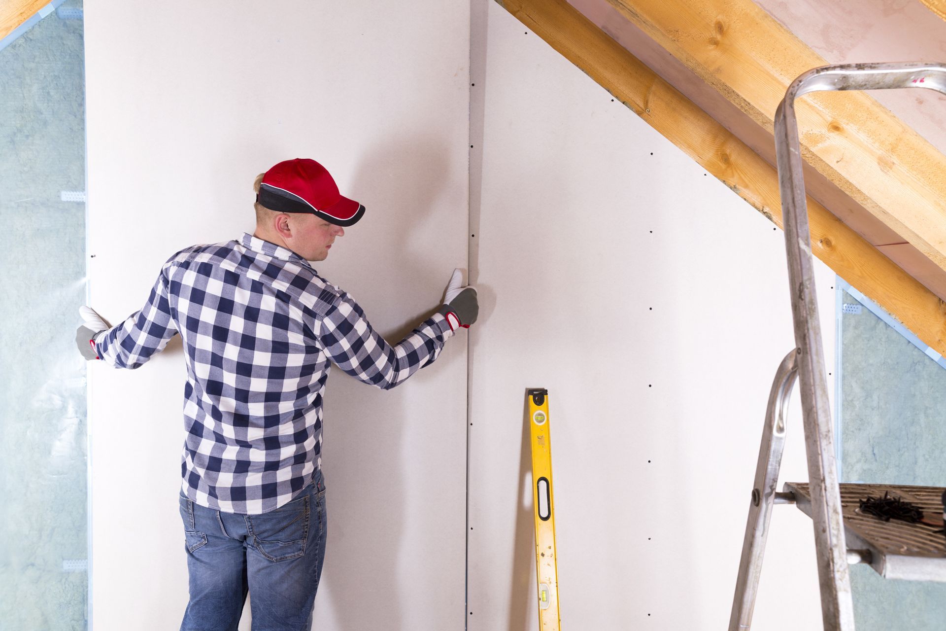 Man in a plaid shirt and cap installing drywall