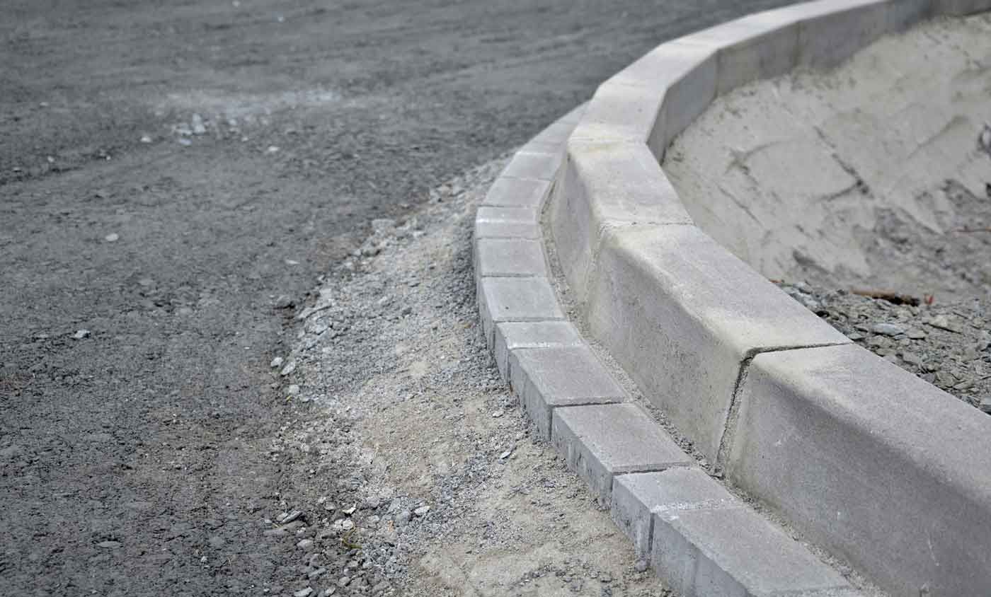 Curved concrete curb bordering a gravel surface.