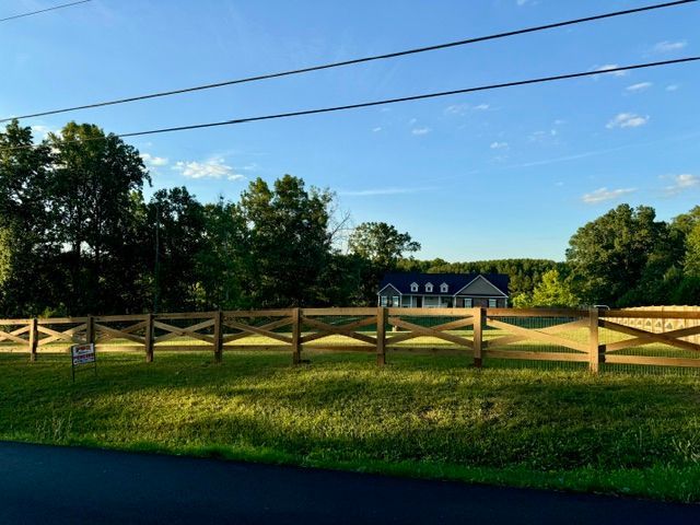 A wooden fence surrounds a grassy field with a house in the background | Scottsville, VA | PBR Grounds LLC