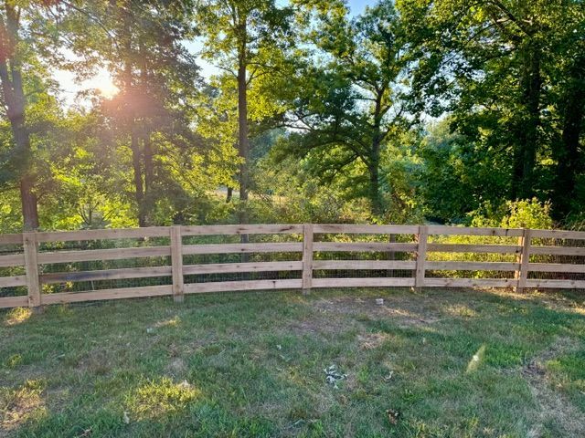 A wooden fence surrounds a grassy field with trees in the background | Scottsville, VA | PBR Grounds LLC