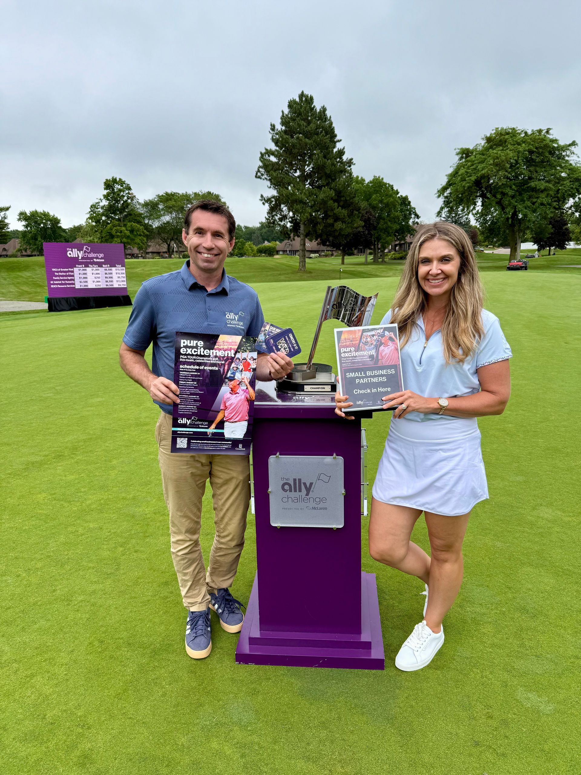 A man and a woman are standing next to each other on a golf course holding magazines.