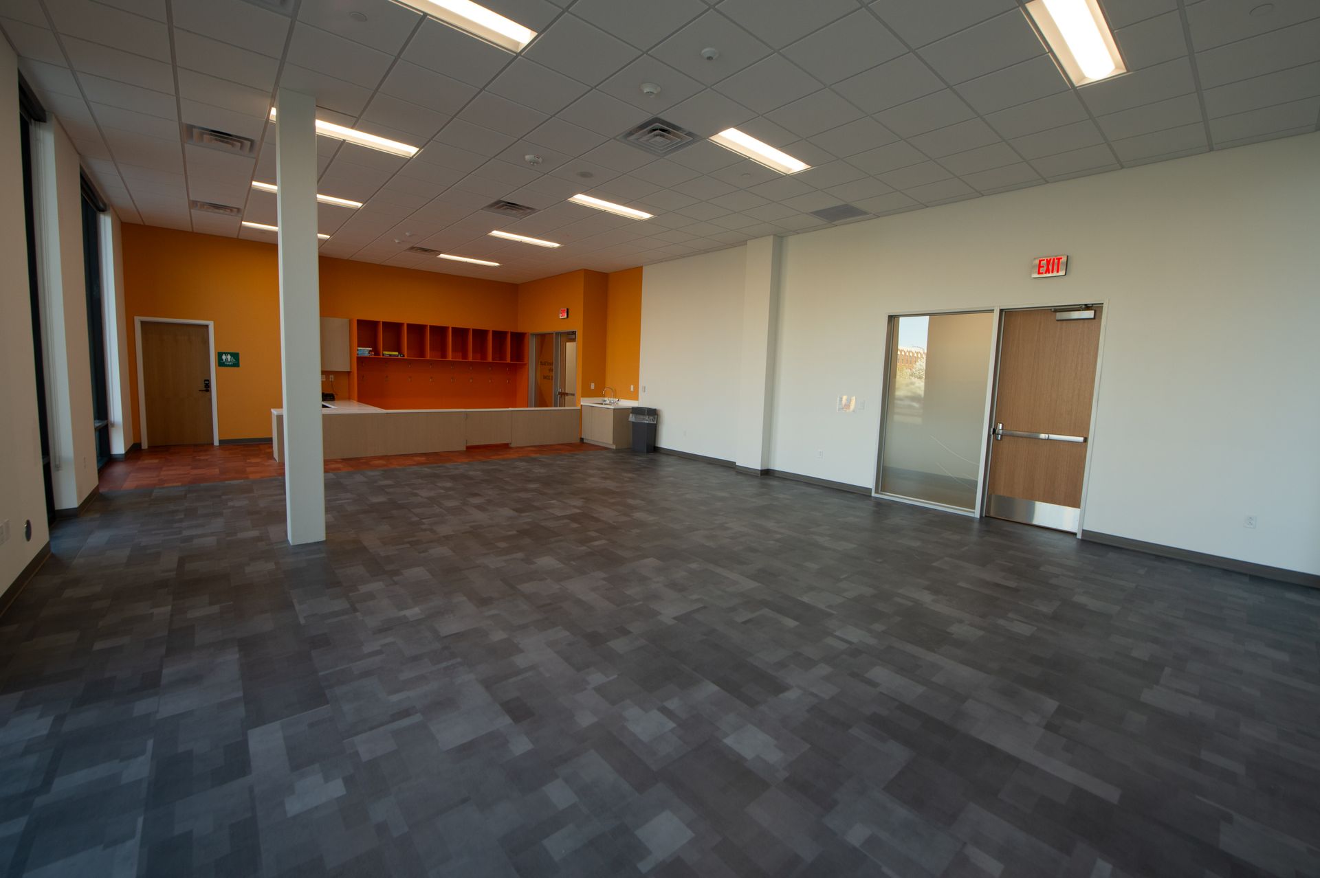 A large empty room with a tiled floor and a red exit sign