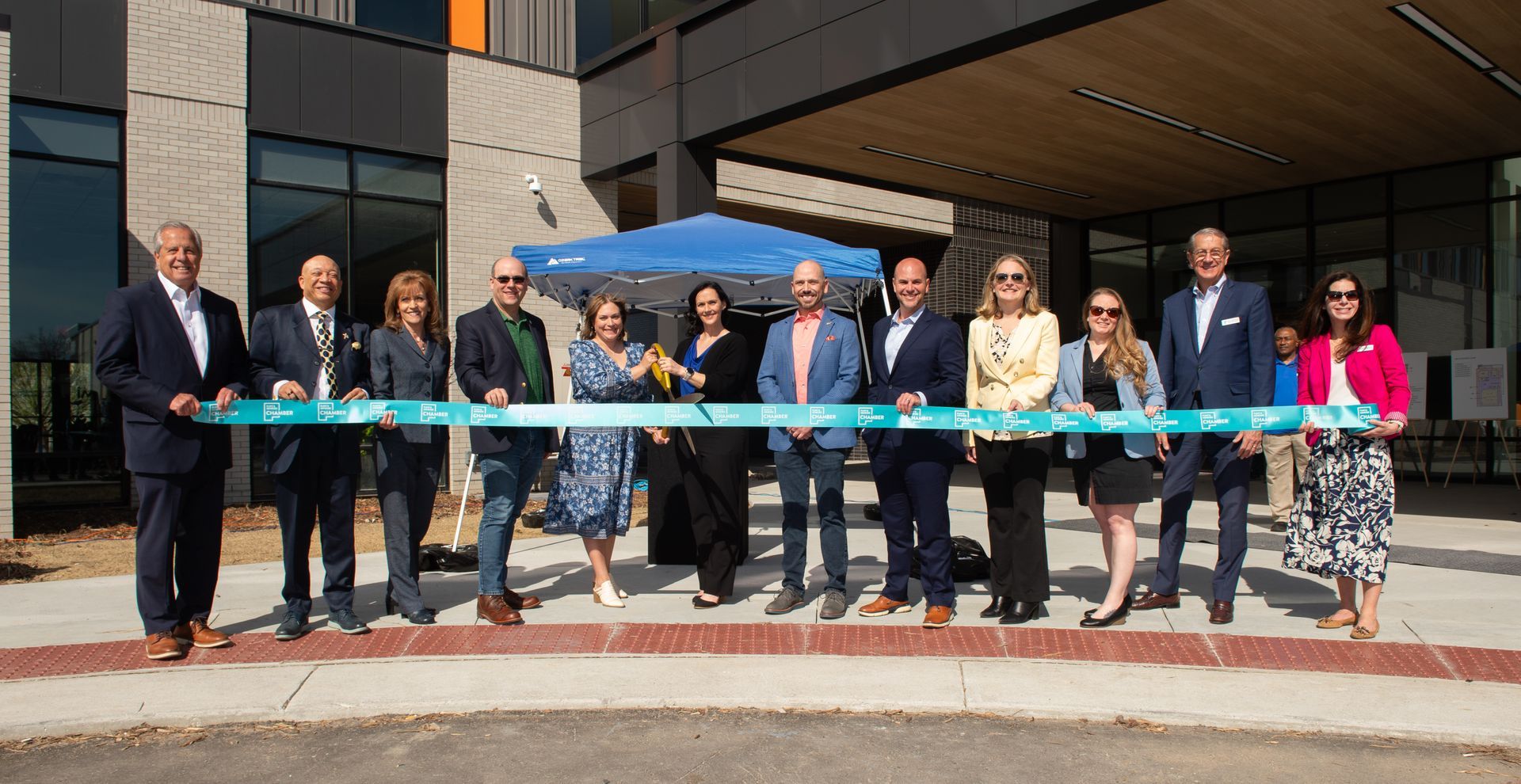 A group of people are standing in front of a building cutting a ribbon.