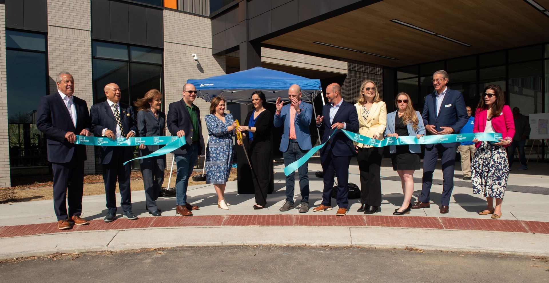 A group of people are standing in front of a building cutting a ribbon.