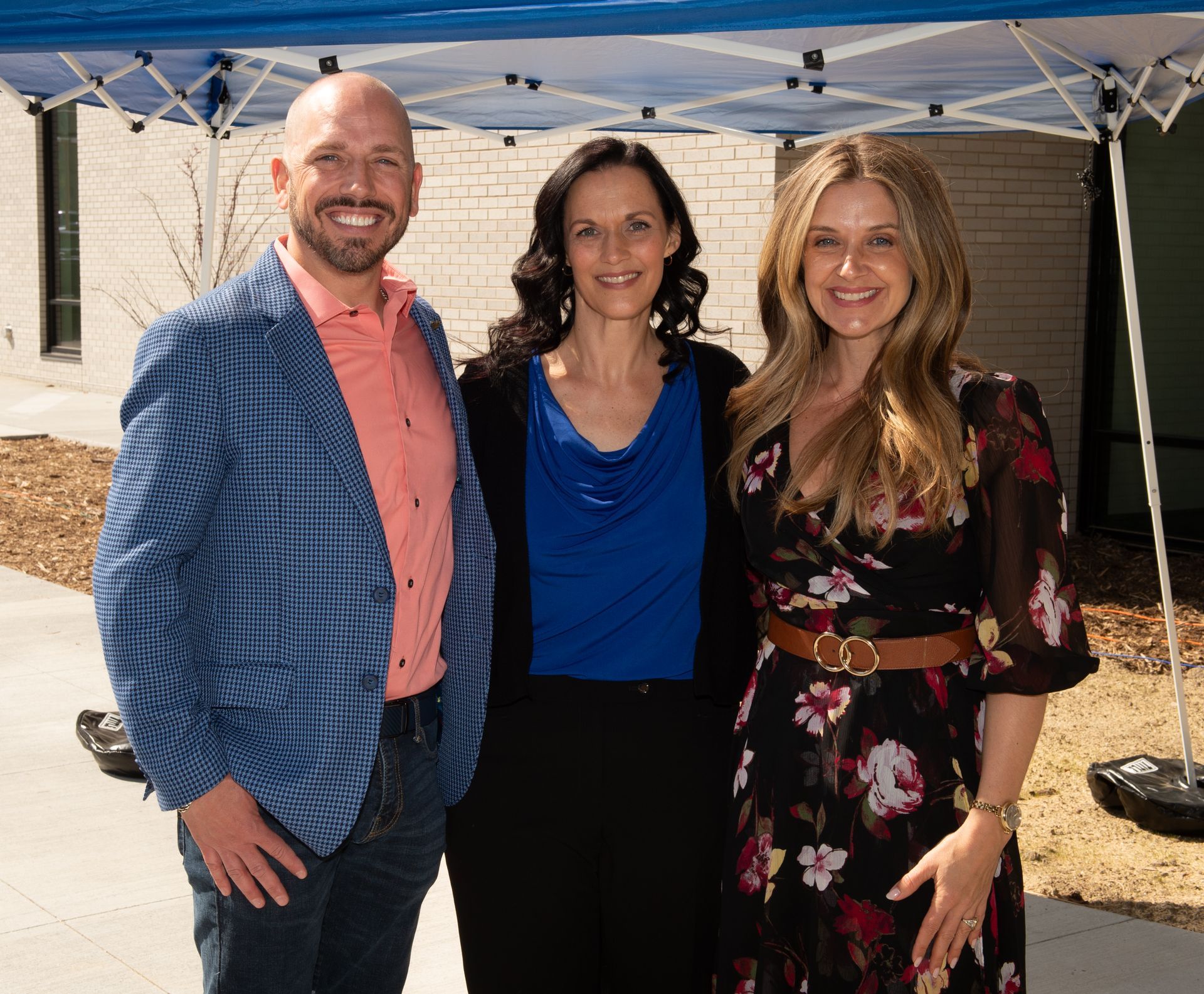 A man and two women are posing for a picture under a tent.
