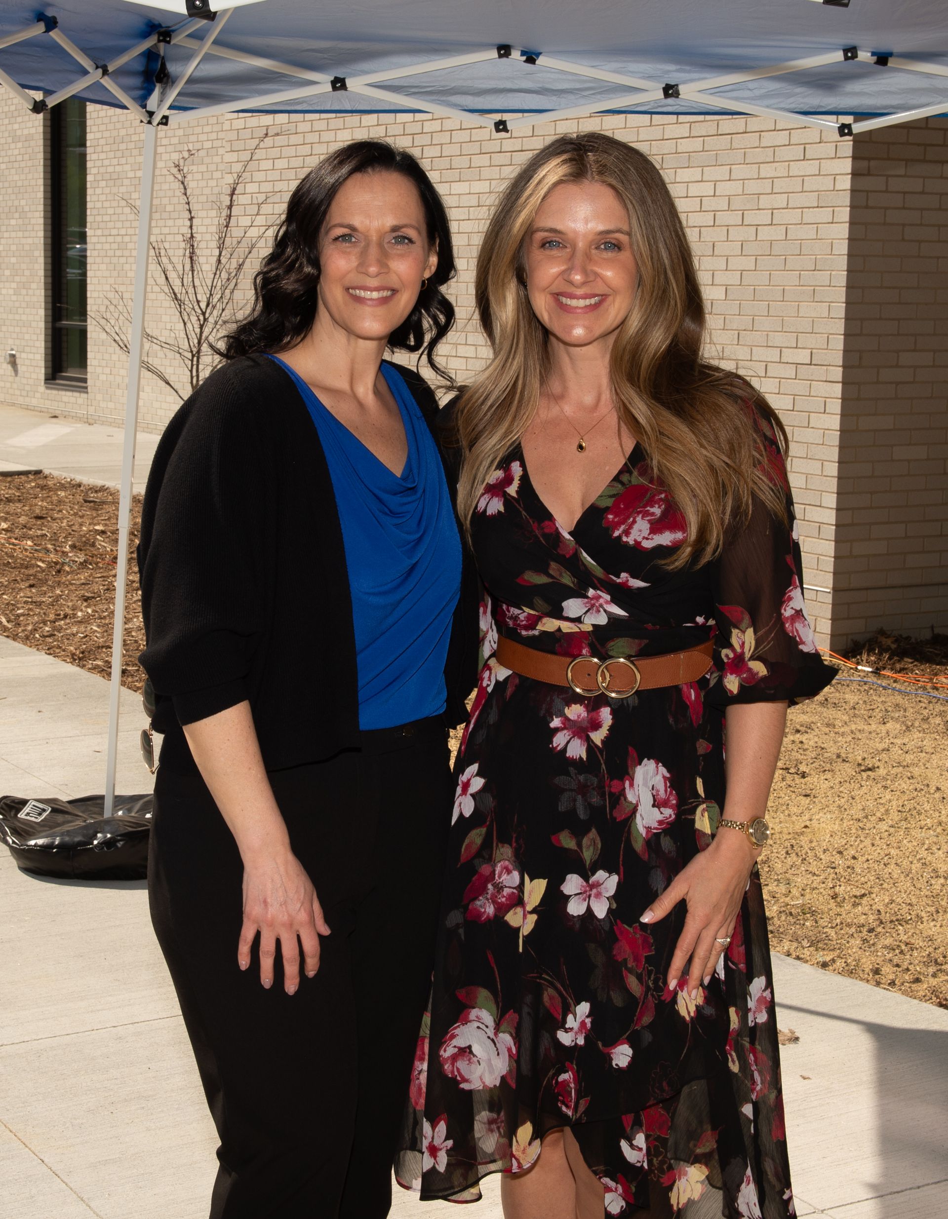 Two women are posing for a picture in front of a tent.