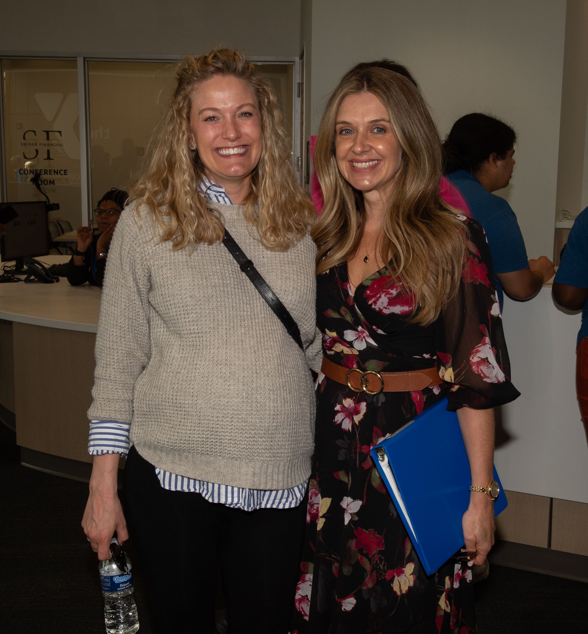 Two women are posing for a picture and one is holding a blue folder