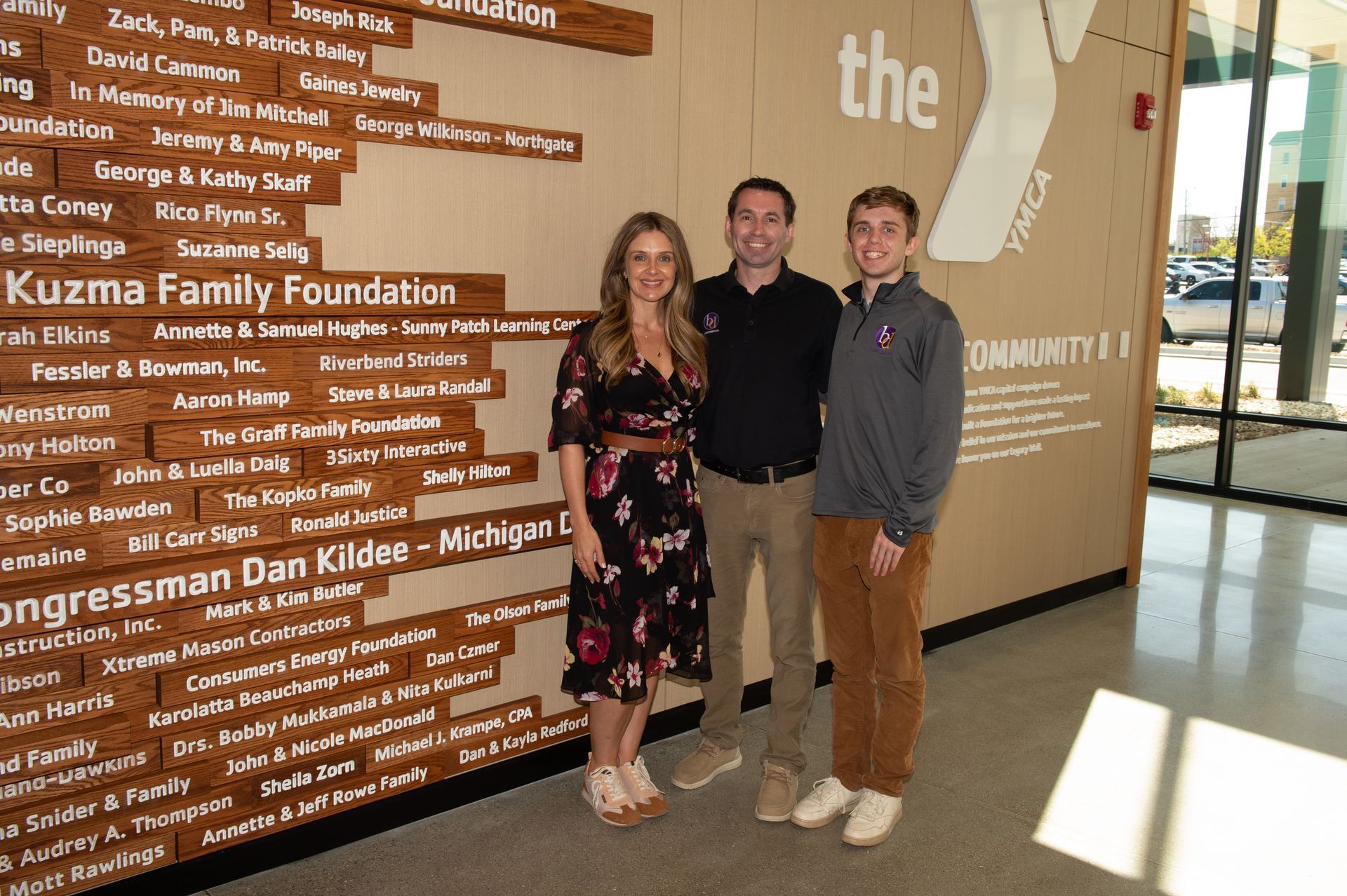Three people are posing for a picture in front of a wall that says the y.