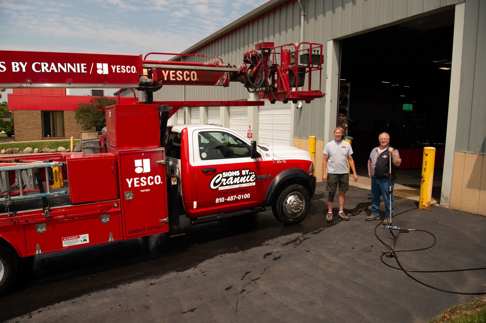 Two men standing next to a red truck that says yesco