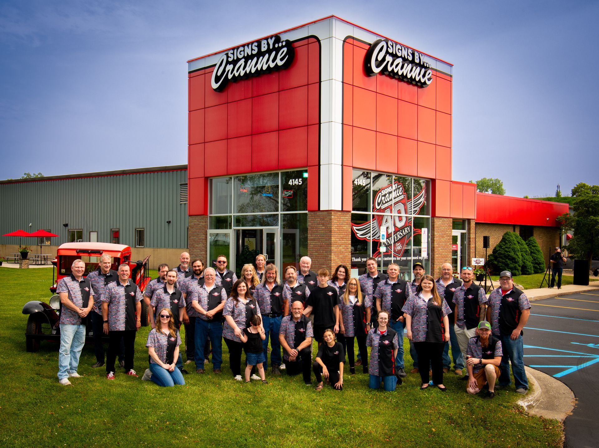 A large group of people are posing for a picture in front of a building that says Sign's by Crannie on it