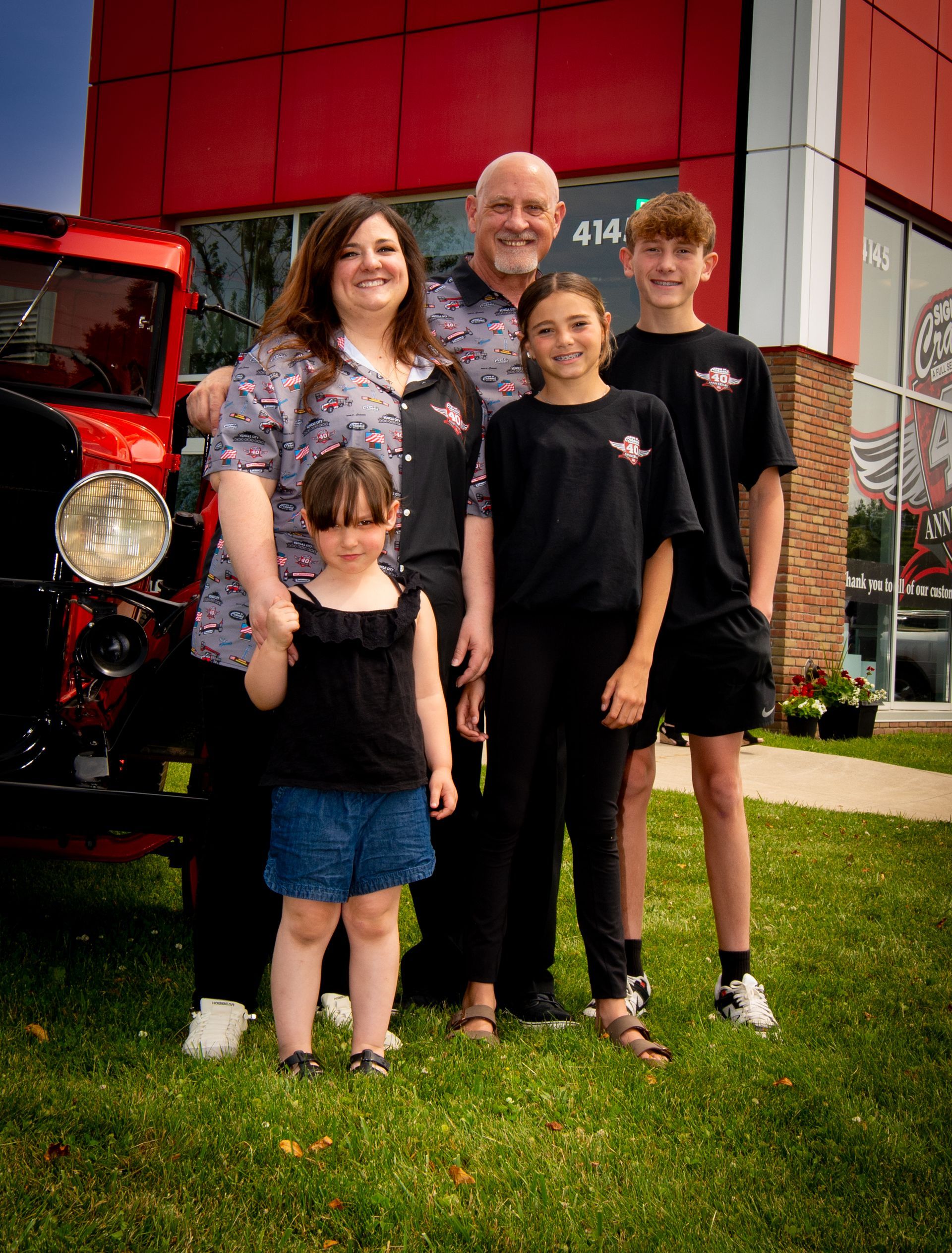 A family is posing for a picture in front of a red truck.