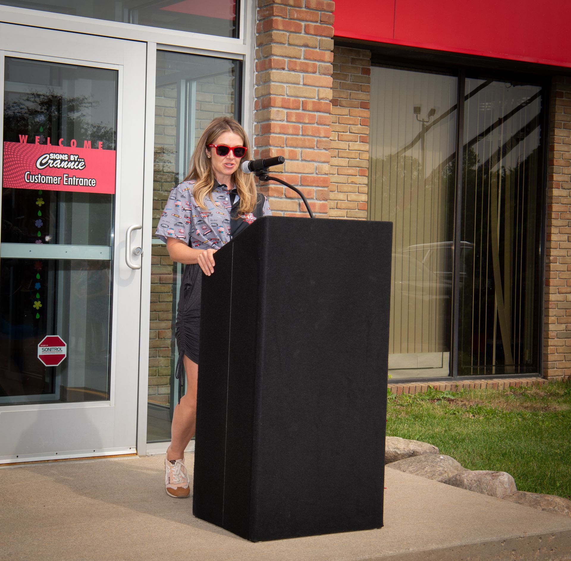 A woman stands at a podium in front of a building that says ' Crannie's ' on it