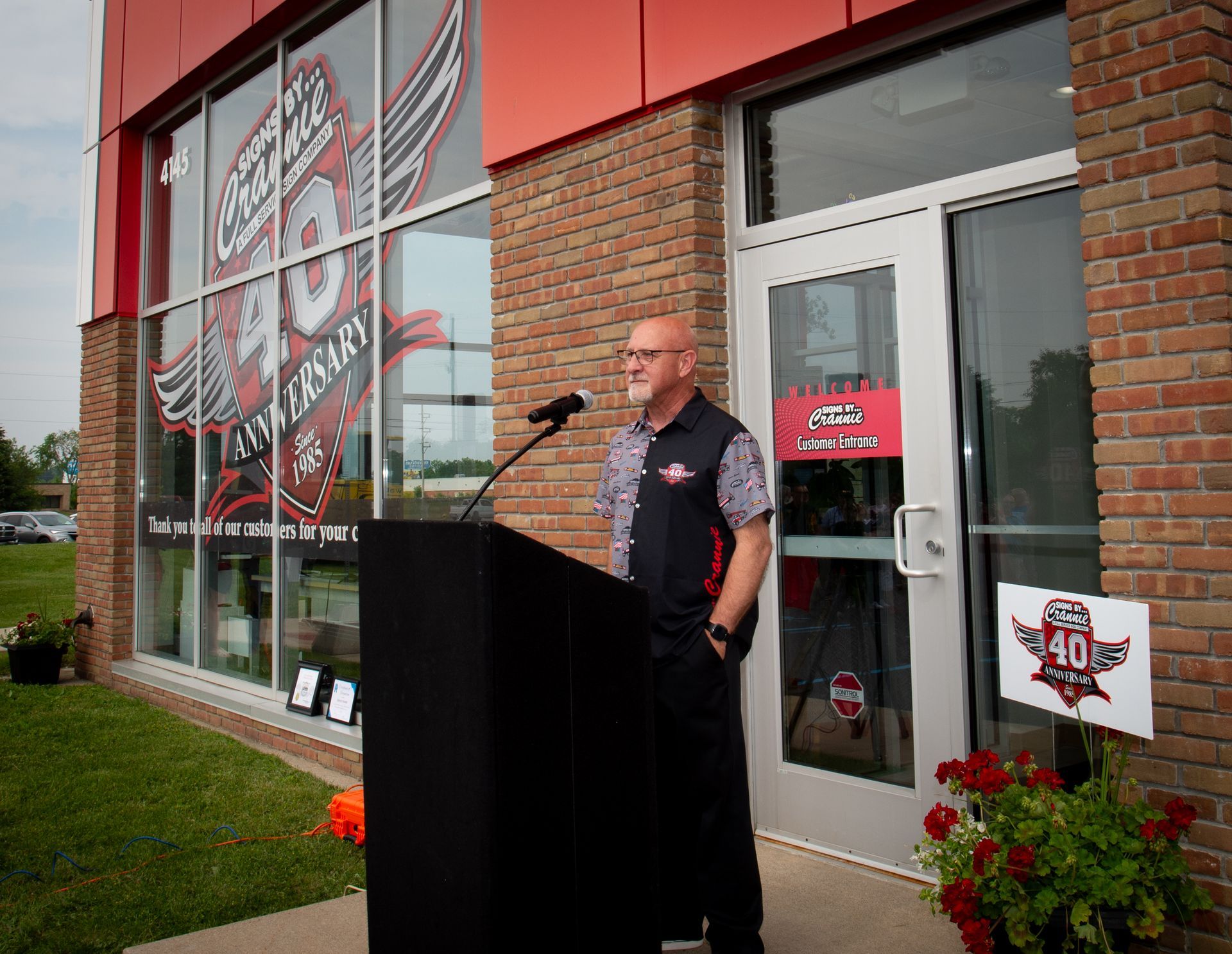 A man is giving a speech at a podium in front of a brick building.