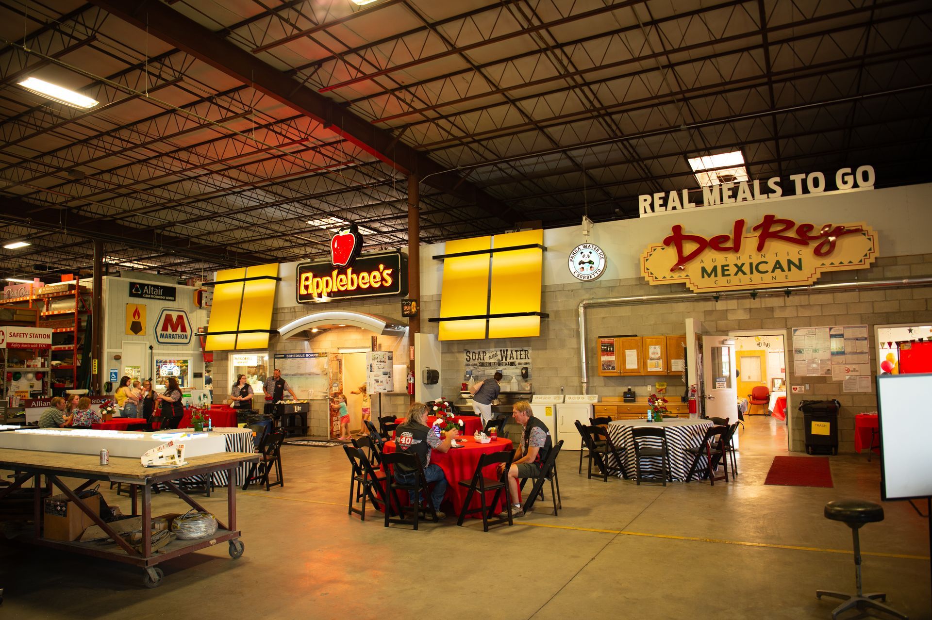 A group of people are sitting at tables in front of a sign that says real meals to go