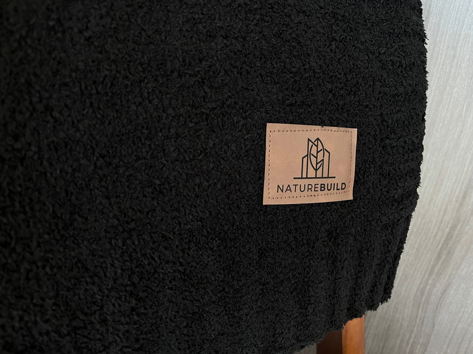 A black stool with a label on it is sitting on a wooden floor.