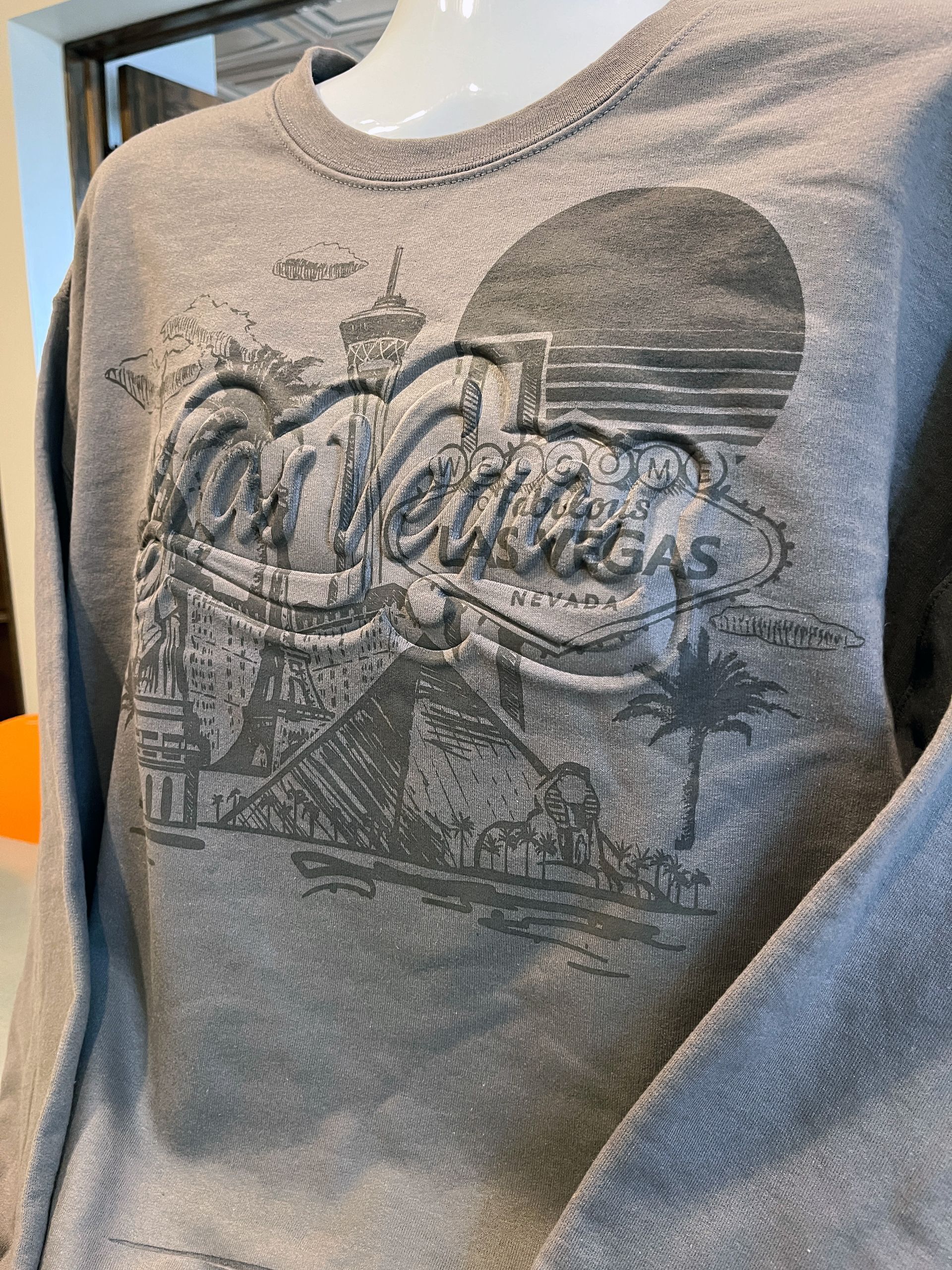 Closeup of gray sweatshirt with embossed script text reading Las Vegas