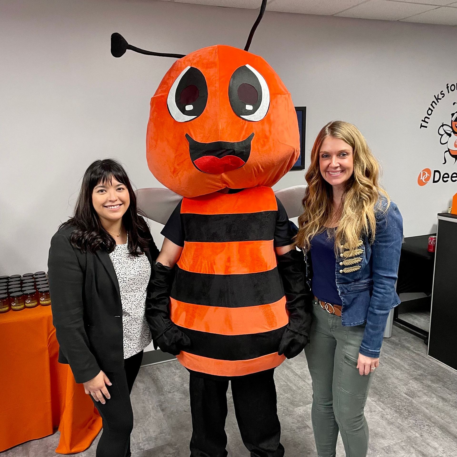 Two women standing next to an orange and black bee mascot